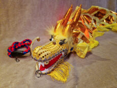 Tuotekuva Kotae Expon myymästä keltaisesta 3 metriä pitkästä poi-lohikäärmeestä. keltainen ja kultainen häntäinen poi-lohikäärme keltaisilla suomukuviolla ja kultakoristepisteillä. Lohikäärmeellä on pitkät rautalanka viikset, joiden päässä on kulkuset. sekä poi-lohikäärme beigellä pörröisellä taustalla. Poi-lohikäärmeen vieressä on punasininen pyöritykseen käytettävä hihna.